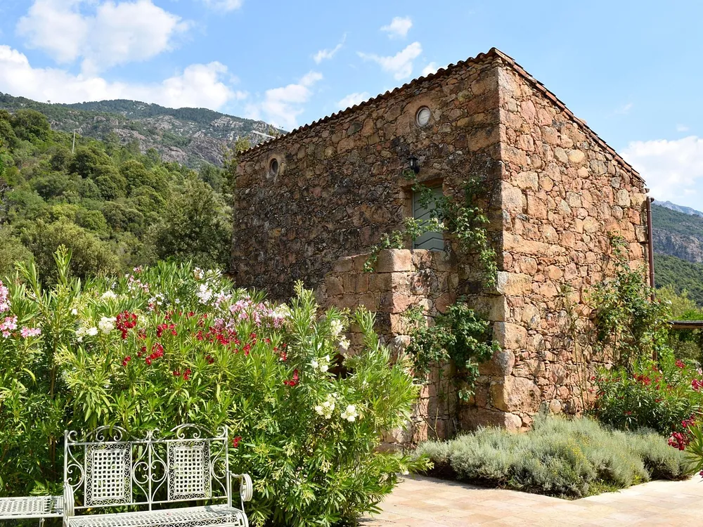 Une maison de pierre entourée de fleurs
