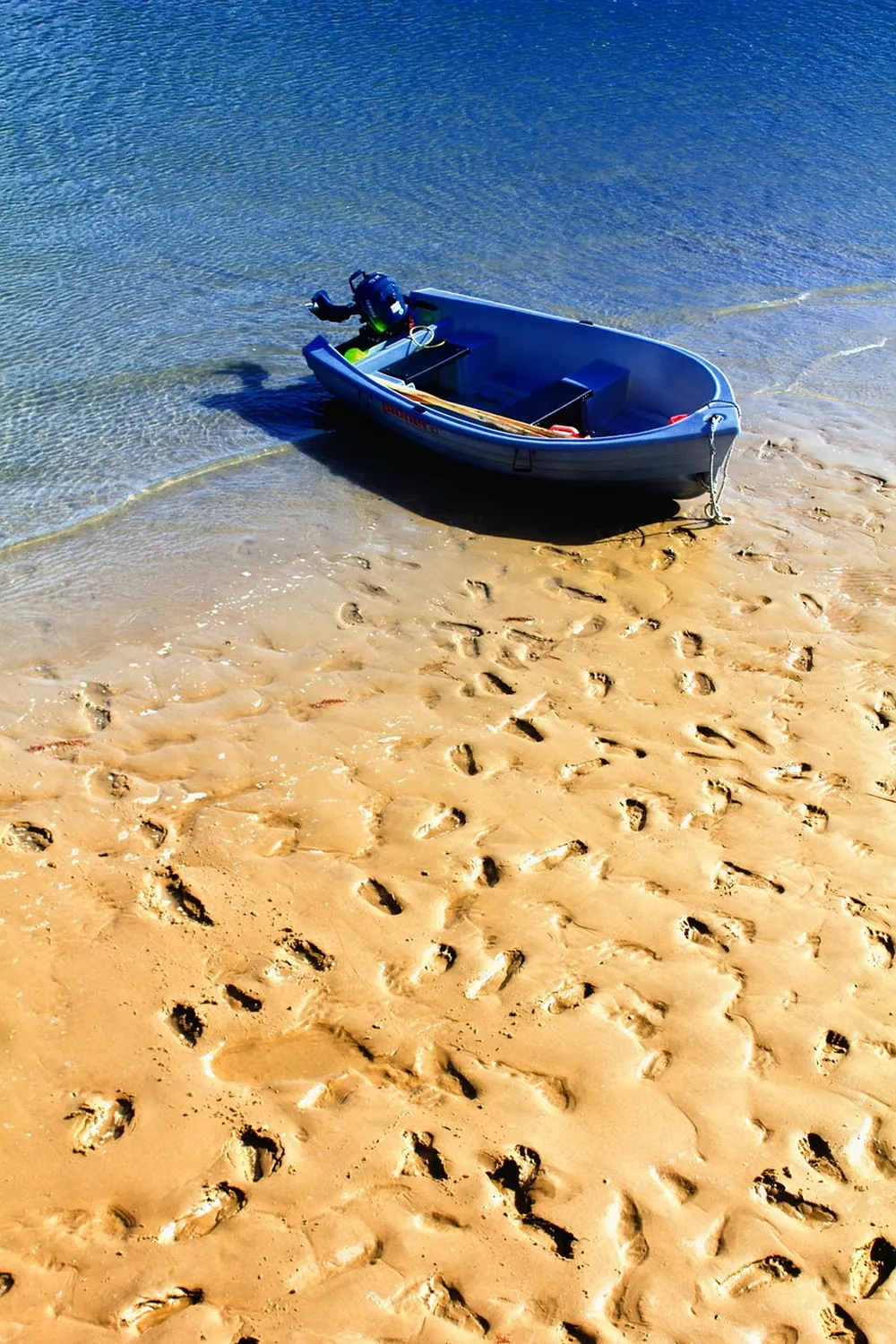 Une barque bleue tirée sur le sable, au bord de l'eau