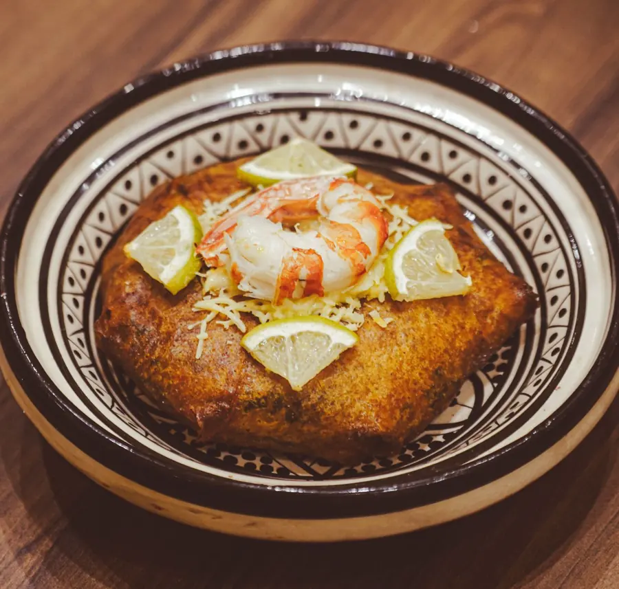 Pastilla dorée garnie d'une crevette, de fromage râpé et de quartiers de citron vert